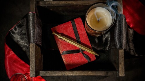 Smoke drafts from a recently snuffed candle, nestled with a notebook and pen inside a dark wooden box.