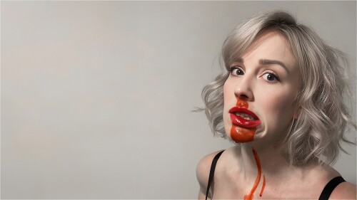 Tegan Verheul's face against a grey background. She has curly blonde hair and a bloody nose.