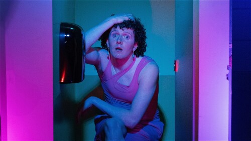 - Three toilet cubicles in colours: pink, green/blue and purple. - Cubicle one (left): A man (Ollie) dangling off the door with a mahoosive smile on his face. - Cubicle two (middle): Ollie sat on the toilet seat with his legs crossed and his hand on his 