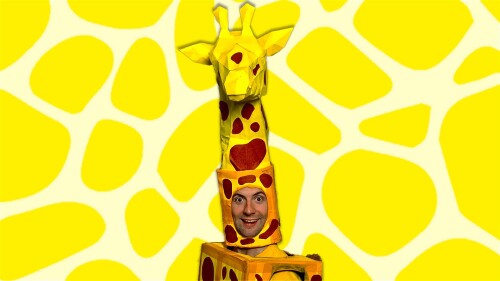 A smiling person in a Giraffe costume, in front of a yellow Giraffe patterned background.