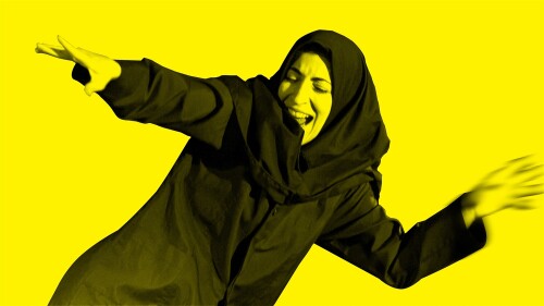 Sara, an Iranian women with light olive skin is dressed in a dark blue Iranian girls school uniform (blazer, trousers & headscarf). She smiles like a cheshire cat, dancing, with her arms out to her side. The image is edited with a bright Yellow filter.