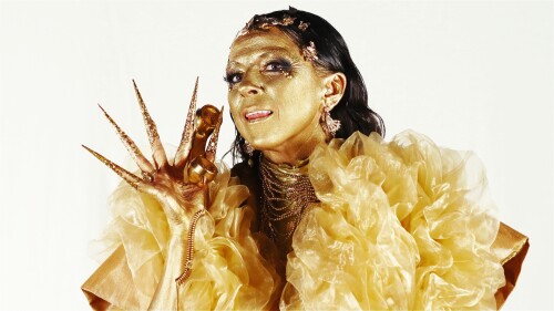 Kat McGarr dressed all in gold, skin and all, holds up a gold telephone.
