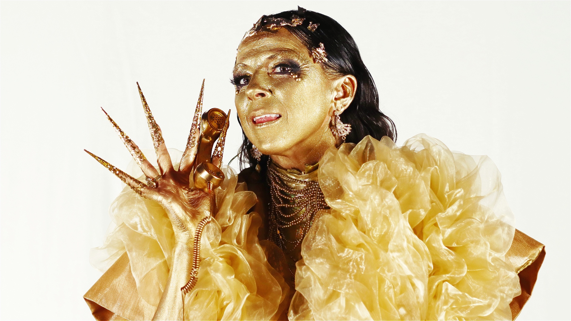 Kat McGarr dressed all in gold, skin and all, holds up a gold telephone.