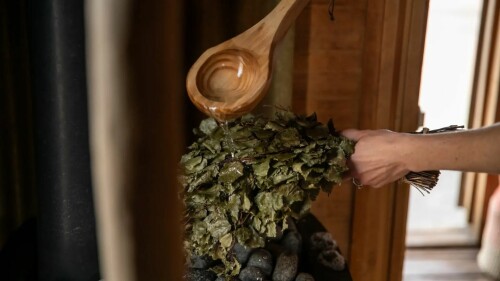 A wooden spoon being poured onto a bunch of greenery, there are sauna stones underneath. 