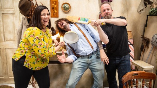 Talking Bottom hosts Angela Pearson, Mat Brooks and Paul Tanter are pictured mucking around on the set of the Bottom Exposed UK TV documentary. On the left a smiling Angela is brandishing a frying pan, on the right Paul is poised holding a cricket bat. I