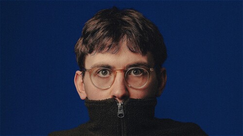 Tim Reeves, a white man with short brown hair and glasses looks directly at the viewer. His mouth is covered by the neck of his fleece.