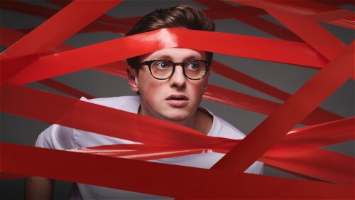 Man in a white t-shirt is entangled in multiple strips of red tape.