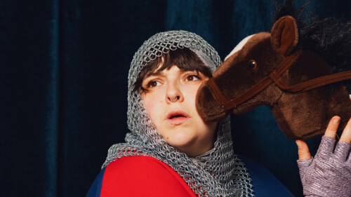 A photo of a woman wearing a knight's costume and hugging a toy horse 
