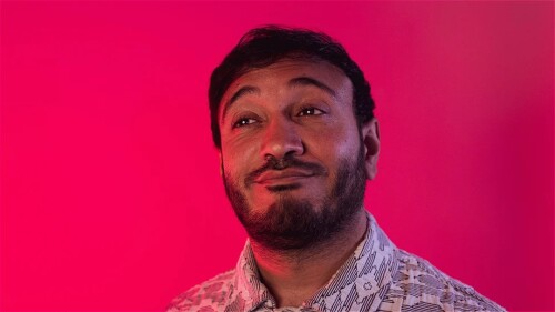 A photo of Bilal zafar doing a weird face against a pink backdrop. 