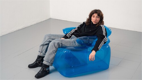 A woman with brown hair wearing a black sports jacket and jeans is leaning back on a blue inflatable chair