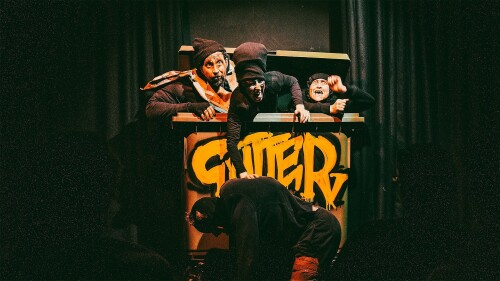 A filthy troupe of bouffon clowns emerge from a large bin