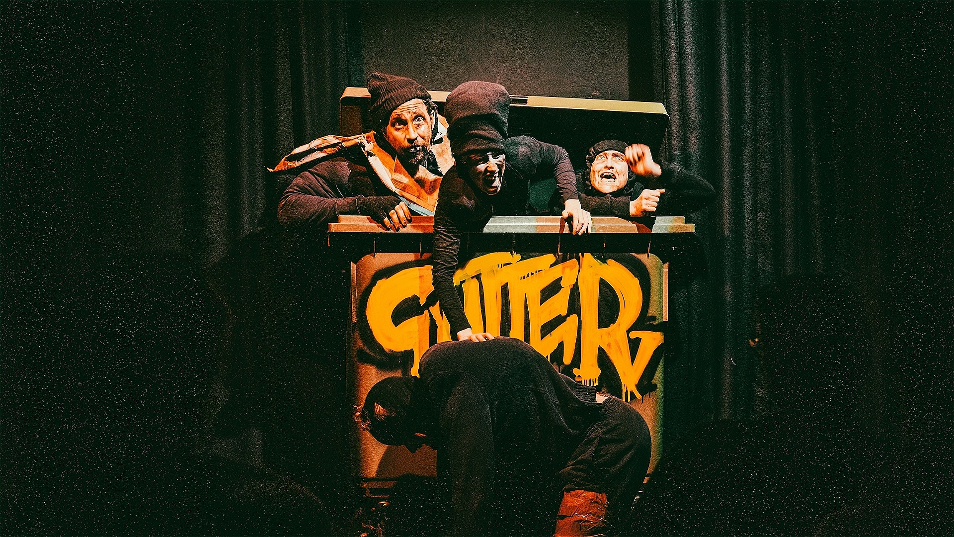 A filthy troupe of bouffon clowns emerge from a large bin