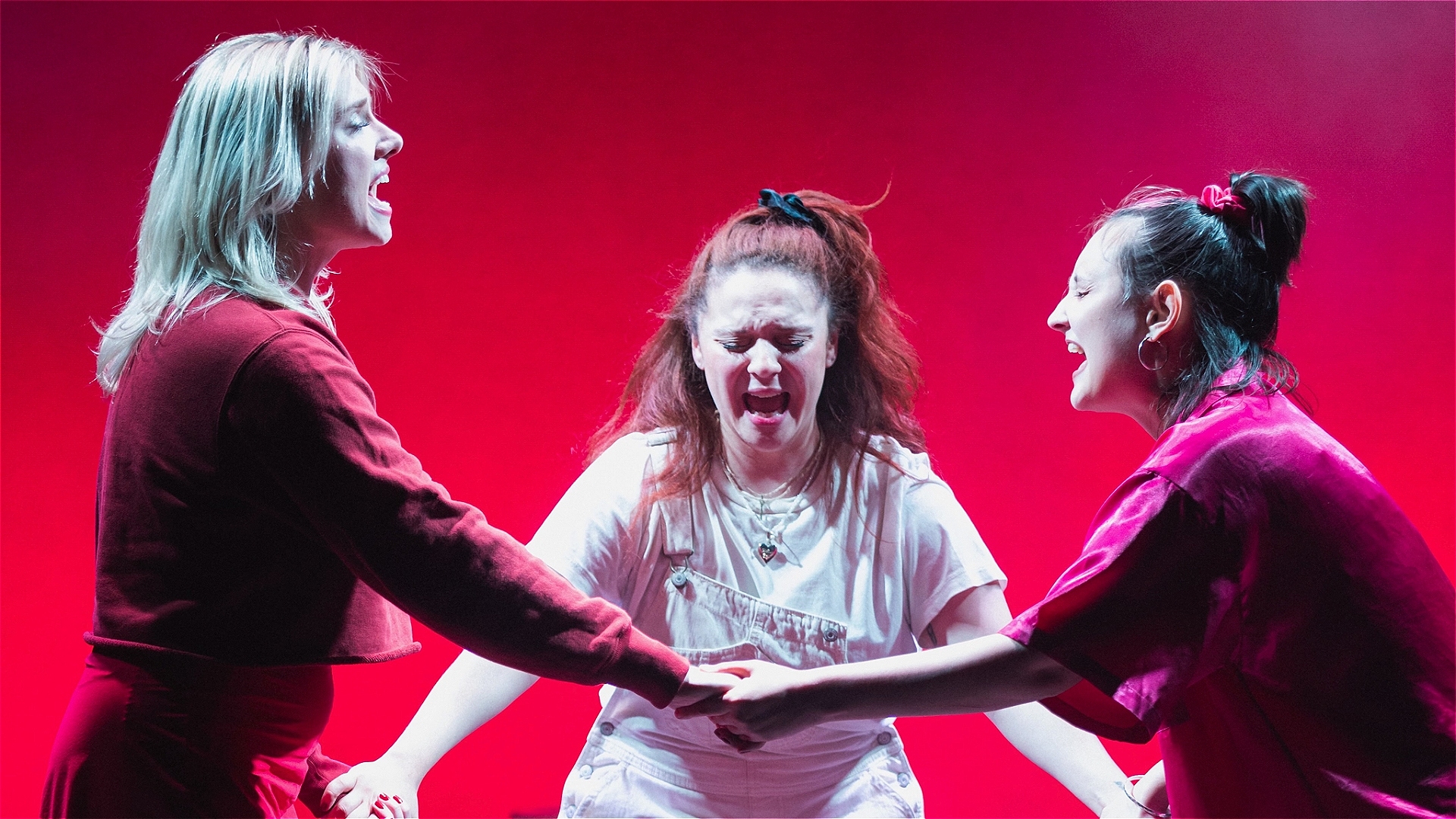 Three girls hold hands in a circle, looking like they're yelling or chanting