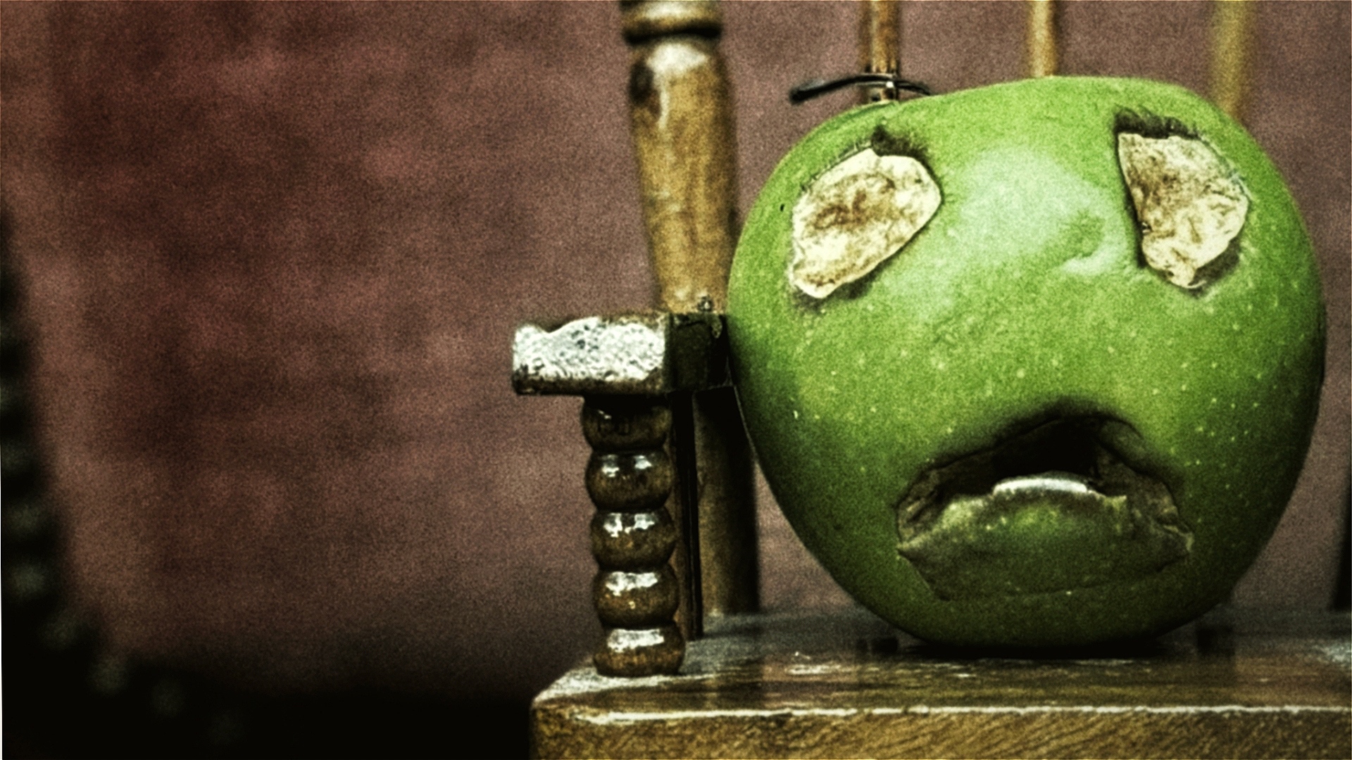 A green apple sits on a wooden rocking chair. Two eyes and a mouth have been bitten out of her.