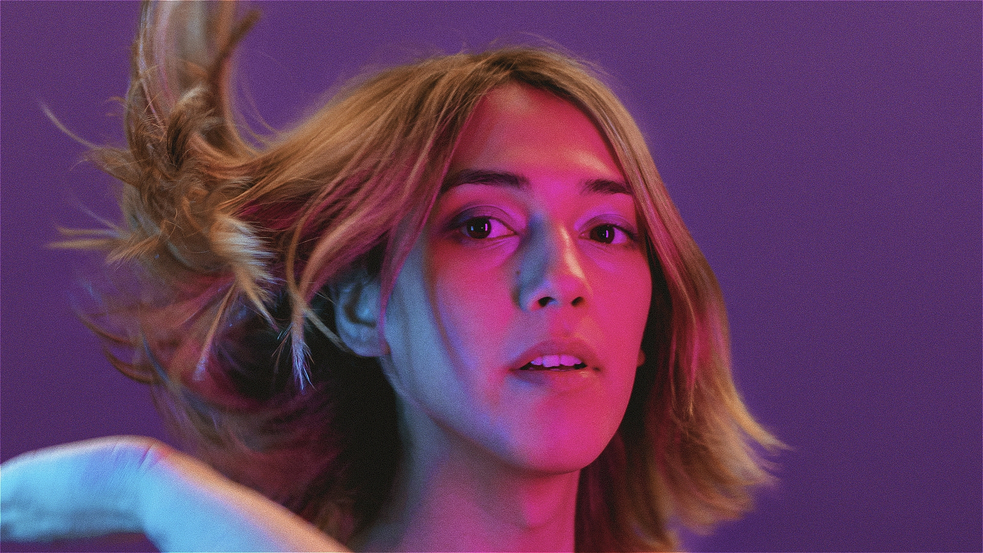 A woman (Alex) in pink and blue lighting, flipping her blonde hair out to the left.