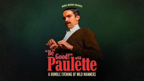 A peculiar gentleman with a big mustache and slicked down, parted hair stands cautiously against a dark green background.