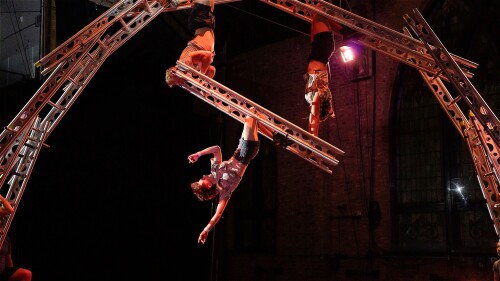 6 circus artists balance and manipulate 6 large ladders.