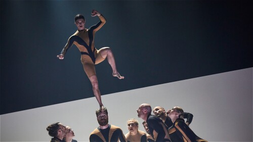 Image of female performer in a cropped bodysuit standing on a male performers head.