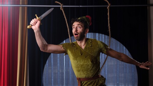 Performer Gianmarco wears a peter pan costume and holds up a toy sword in the air