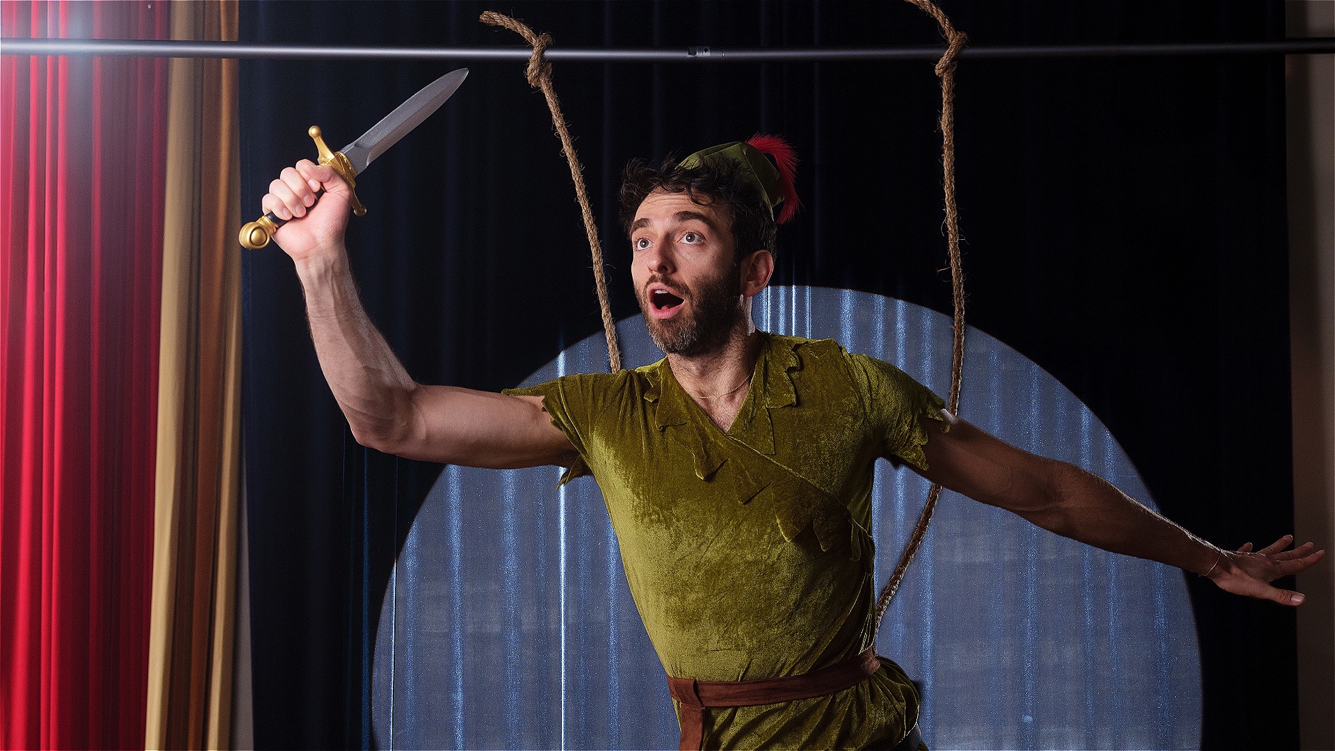 Performer Gianmarco wears a peter pan costume and holds up a toy sword in the air