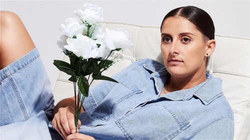 A woman in denim lying on a couch holding flowers