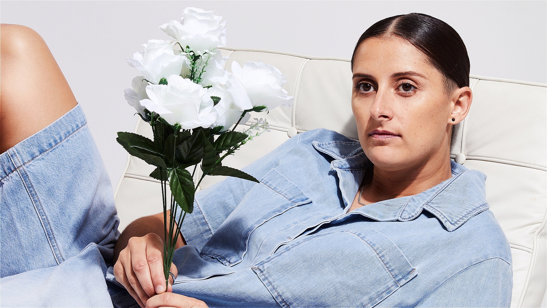 A woman in denim lying on a couch holding flowers