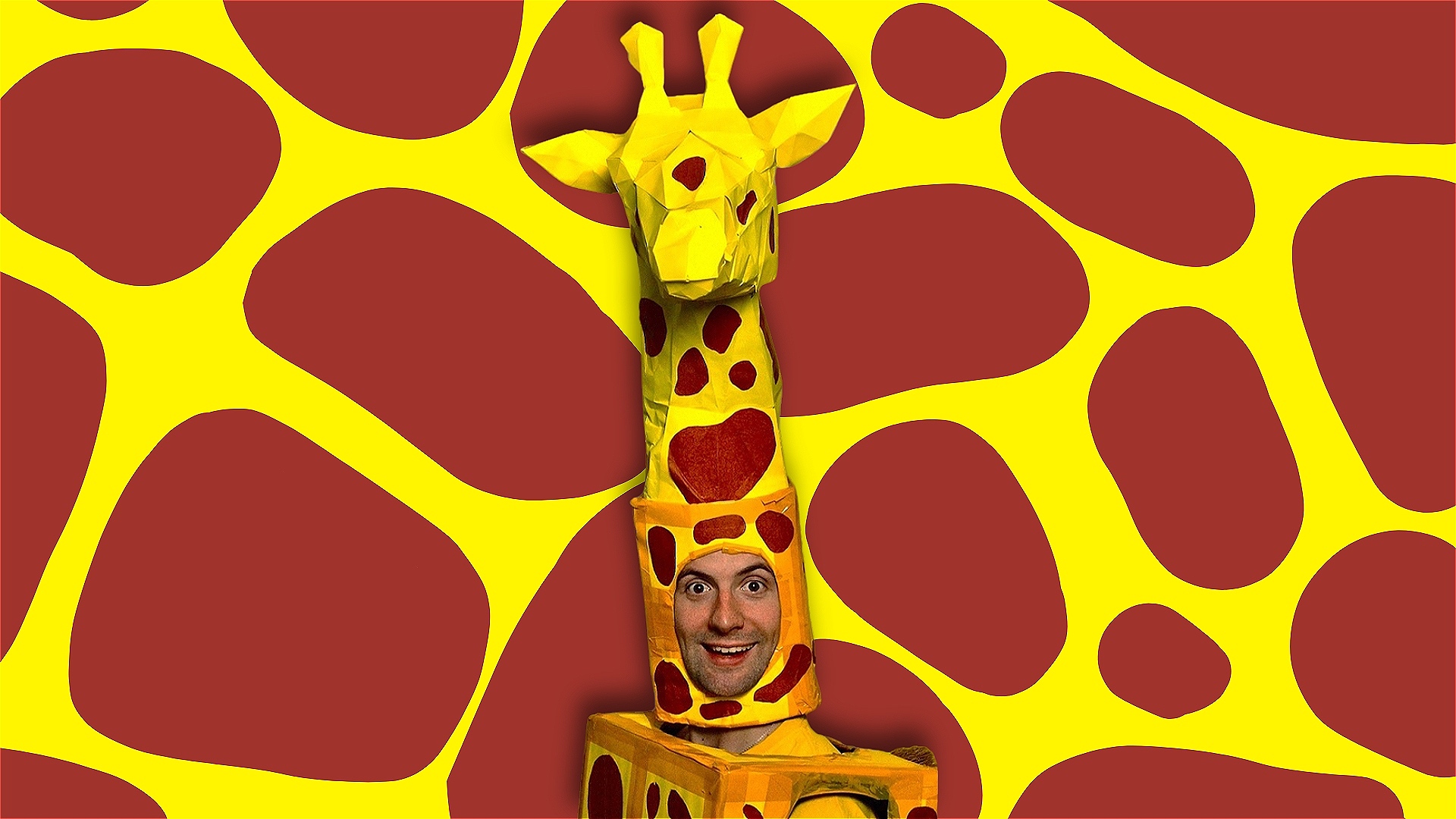 A smiling person in a Giraffe costume, in front of a Giraffe patterned background.