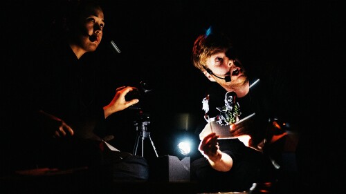 Two puppeteers operate shadow puppets.