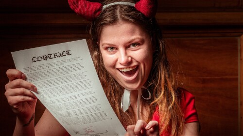 Actor Alex Medland, dressed as the devil with red horns and a grin to match, takes a lit match to a contract signed by 'Faustus.'