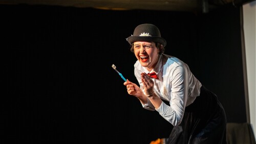 A woman in a white shirt, black skirt and red bowtie is clapping with an extremely excited face.
