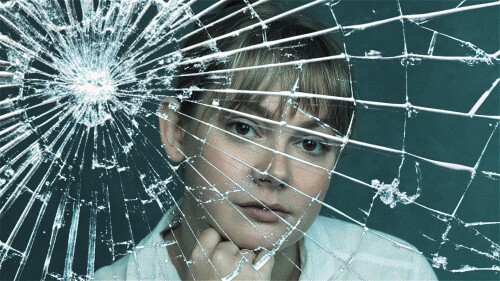 Performer looks at audience through grass cracked window 