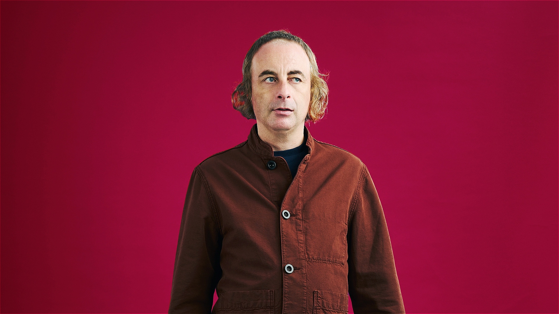 Paul foot stands looking curiously against a red background 