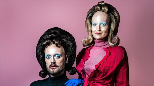 Two strange looking human type characters with enormous foreheads stare into the camera looking slightly sinister. They wear suburban style clothes and huge 60s hair. Think a cross between Stepford wives and Mars Attack.