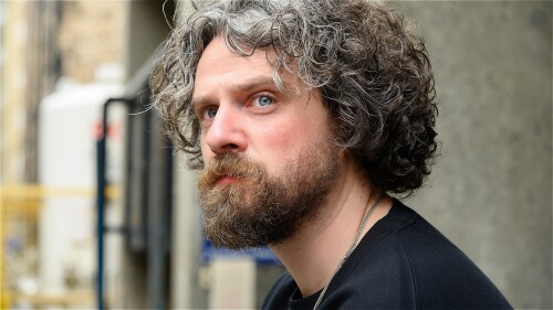 Man with unkempt curly, greying hair and ginger beard