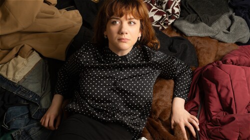 A woman dressed in black props herself up in a pile coats.