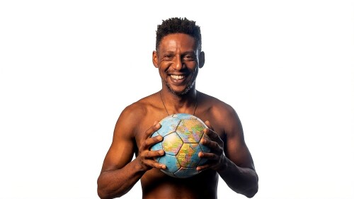 The image shows the actor Ícaro Negroni, a dark-skinned man, with a smile on his face. He is shirtless and holding a soccer ball with both hands with an image of the globe in it.