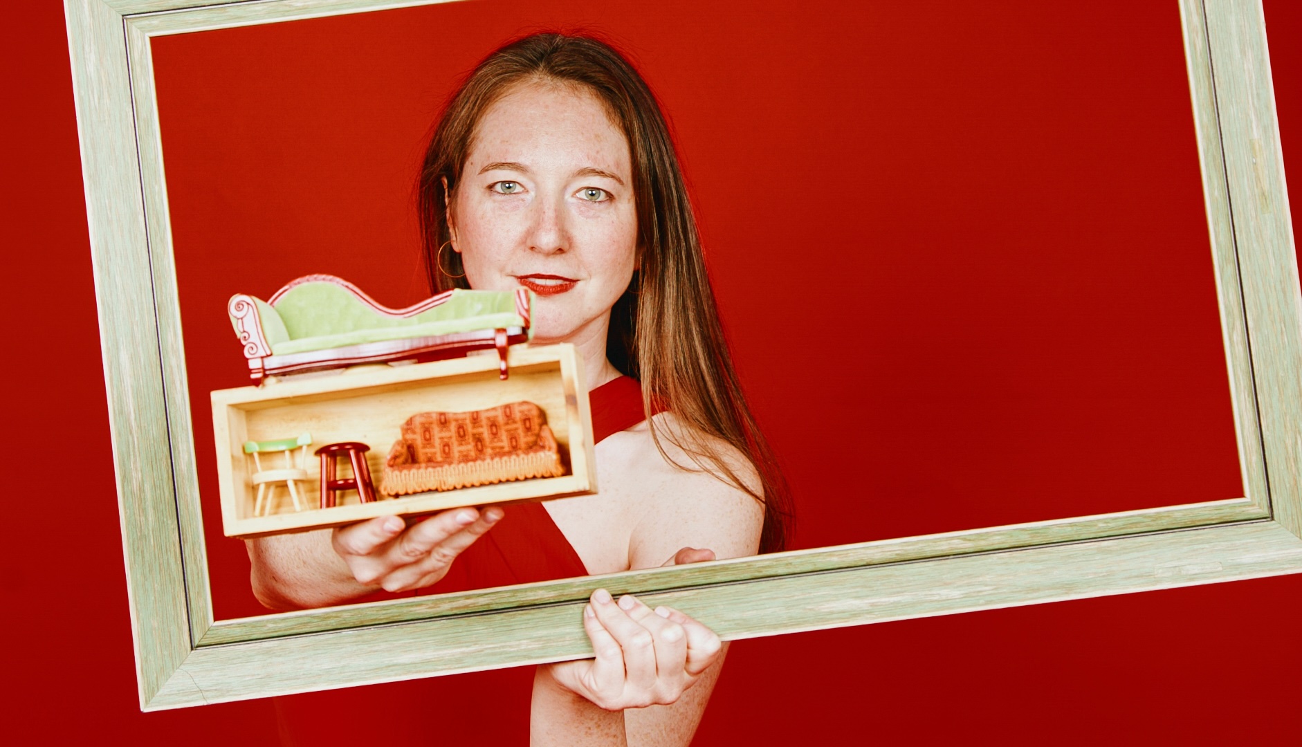 a woman stands in a frame against a red background holding some tony furniture